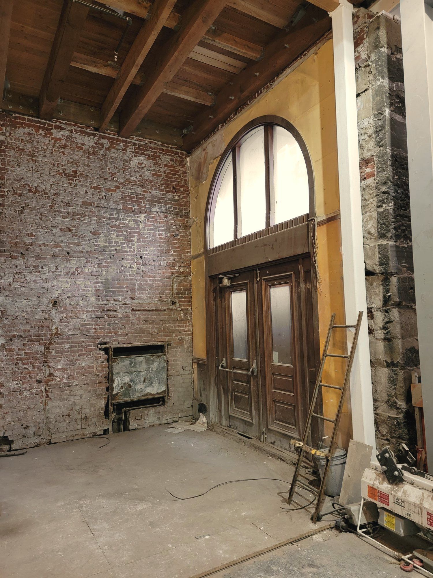 A brick and timber commercial interior under renovation, with a tall arched window.